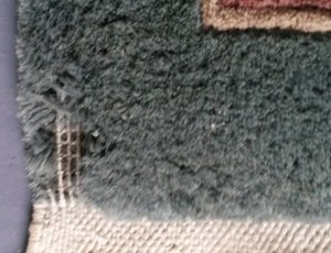 This shows a corner of a Chinese rug that was under a sofa that has been eaten away by succesive moths to the point where you can see the cotton backing