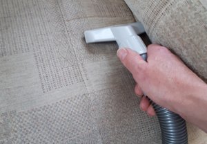 Using a hand tool to dry vacuum an armchair before cleaning